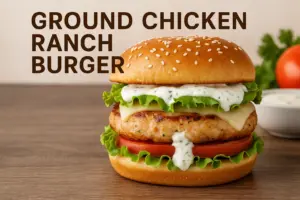 Ground Chicken Ranch Burger with lettuce, tomato, ranch dressing, and sesame bun on wooden table.